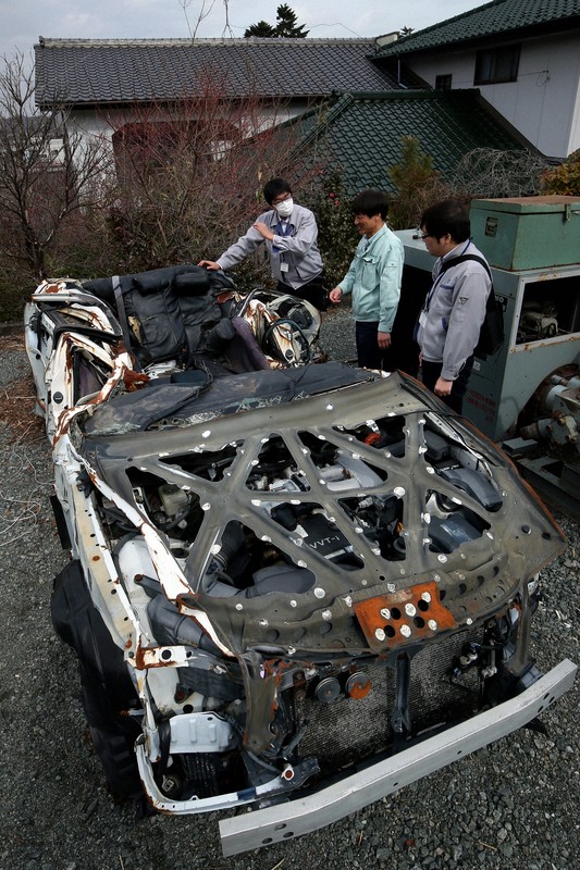 津波にの襲われて大破し、自動車整備工場に保管中のパトカーに触れる富岡町の職員ら。展示を前に保存処理が行われた＝福島県の同町で2015年2月25日、森田剛史撮影