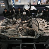 避難誘導中、津波に襲われて殉職した2人の警察官が乗っていたパトカーの前で説明を聞く、いわき市から訪れた高校生ら＝福島県富岡町のとみおかアーカイブミュージアムで2024年2月1日、手塚耕一郎撮影