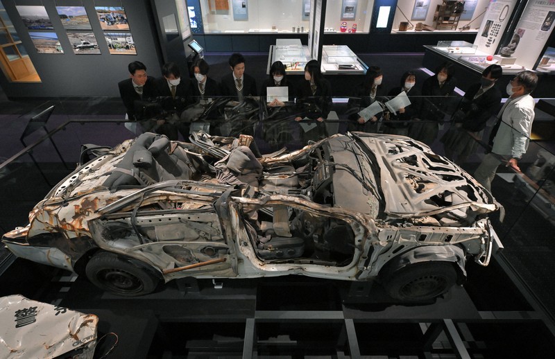 避難誘導中、津波に襲われて殉職した2人の警察官が乗っていたパトカーの前で説明を聞く、いわき市から訪れた高校生ら＝福島県富岡町のとみおかアーカイブミュージアムで2024年2月1日、手塚耕一郎撮影