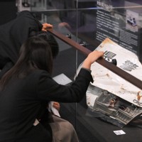 避難誘導中、津波に襲われて殉職した2人の警察官が乗っていたパトカーを見学する、いわき市から訪れた高校生。車両の横には、福島県警察と書かれた壊れたトランクのふたが置かれている＝福島県富岡町のとみおかアーカイブミュージアムで2024年2月1日、手塚耕一郎撮影