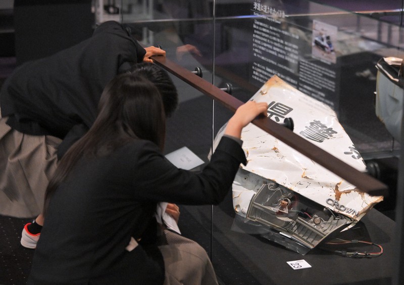 避難誘導中、津波に襲われて殉職した2人の警察官が乗っていたパトカーを見学する、いわき市から訪れた高校生。車両の横には、福島県警察と書かれた壊れたトランクのふたが置かれている＝福島県富岡町のとみおかアーカイブミュージアムで2024年2月1日、手塚耕一郎撮影