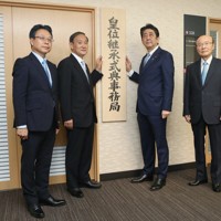 皇位継承式典事務局の看板を掛ける安倍晋三首相（中央右）と菅義偉官房長官（同左）。左端は山崎重孝事務局長、右端は杉田和博官房副長官（肩書はいずれも当時）＝内閣府で2018年8月1日（代表撮影）