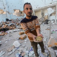 イスラエル軍の攻撃を受けた支援物資の倉庫跡で、パスタを手に持つ男性＝パレスチナ自治区ガザ地区で2024年3月14日、ロイター