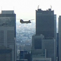 バイデン米大統領の随行者らを輸送するため、東京・西新宿のビル群手前を通過する米陸軍の大型ヘリ「チヌーク」。高度を落としながら六本木の米軍ヘリポートに向かった＝2022年5月22日午後5時39分ごろ、取材班撮影（写真は動画から）