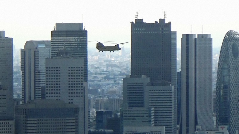 バイデン米大統領の随行者らを輸送するため、東京・西新宿のビル群手前を通過する米陸軍の大型ヘリ「チヌーク」。高度を落としながら六本木の米軍ヘリポートに向かった＝2022年5月22日午後5時39分ごろ、取材班撮影（写真は動画から）