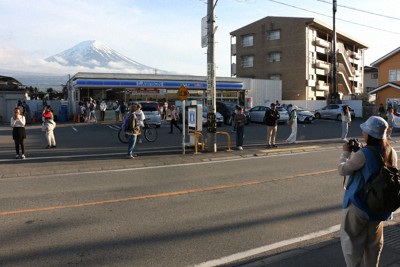 コンビニエンスストアの後ろにそびえる富士山を背景に写真撮影する外国人観光客ら＝山梨県富士河口湖町船津で2024年4月25日午後5時23分、野田樹撮影