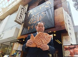 「たいやき ともえ庵」オーナーの辻井啓作さん。持っているのは同店で企画販売しているたい焼きのクッション＝本人提供
