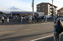 コンビニエンスストアの後ろにそびえる富士山を背景に写真撮影する外国人観光客ら＝山梨県富士河口湖町で2024年4月25日、野田樹撮影　※写真の一部を加工しています