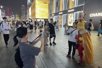 西遊記の孫悟空の仮装をした人と記念撮影する春熙路の観光客＝四川省成都市で2024年7月6日、小倉祥徳撮影