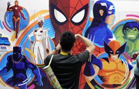 An attendee takes a picture of an illustrated wall of Marvel superhero characters during preview night for Comic-Con International,  July 24, 2024, in San Diego. (AP Photo/Chris Pizzello)