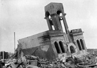 The first floor of the two-storied Shimomura Tokeiten clock shop building is seen crushed, leaving the second floor with arched windows and the clock tower behind. A man and a woman are seen in front of the building. At far right is the Fukuromachi national school (today's Fukuromachi Elementary School). The photo was taken on around Sept. 11, 1945, in Hiroshima's Hiratayacho district (now part of the Hondori area of the city's Naka Ward). (Mainichi/Entaro Yamagami) 