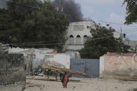 A woman walks on the beach as black smoke is seen rising in the background following an attack in Mogadishu, Somalia, on Aug. 3, 2024. Police in Somalia said Saturday that 32 people died and 63 others were wounded in an attack on a beach hotel in the capital, Mogadishu, the previous evening. (AP Photo/Farah Abdi Warsameh)