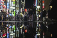 People are reflected in a puddle as they crowd the street in the Kabukicho neighborhood in Shinjuku's  entertainment district in Tokyo, on July 31, 2024. (AP Photo/Kiichiro Sato)