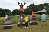 Yuichi Hirako, right, stands in front of his sculptures displayed against the backdrop of a sunflower field at Kasai Rinkai Park in Tokyo's Edogawa Ward on August 1, 2024. (Mainichi/Yuko Murase)