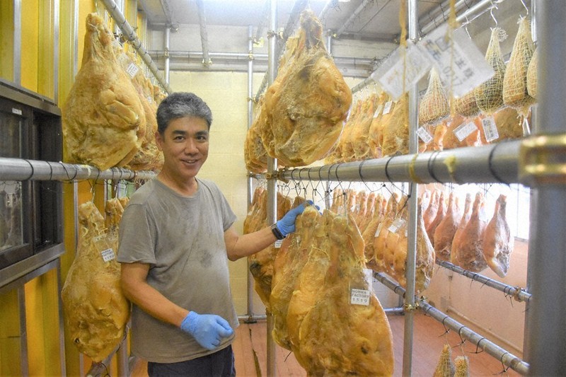 生ハムの原木がつるされた工房で説明する髙橋さん