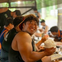 菅平合宿中のバーベキュー大会で大盛りの白飯を手に笑顔を見せる、拓大の村松俊介選手（4年）＝拓大ラグビー部提供　©渡辺周治