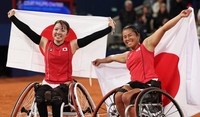 Manami Tanaka, left, and Yui Kamiji raise Japanese flags after winning the women's wheelchair tennis doubles final at the Paris Paralympic Games at the Roland Garros Stadium on Sept. 5, 2024. (Mainichi/Tatsuro Tamaki)
