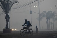A cyclist pedals through the smoke in Brasilia, Brazil, coming from a fire in the environmentally protected area of Brasilia National Park, on Sept. 16, 2024. (AP Photo/Eraldo Peres)