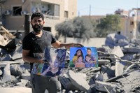 A man carries pictures of his relatives standing at the site of an Israeli airstrike in Saksakieh, south Lebanon, on Sept. 26, 2024. (AP Photo/Mohammed Zaatari)