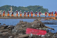 塚田川河口から海に流れ出て堆積（たいせき）した土砂の上で、棒を手に一列に並んで安否不明者を捜索する消防隊員ら＝石川県輪島市で2024年10月1日午前9時12分、手塚耕一郎撮影