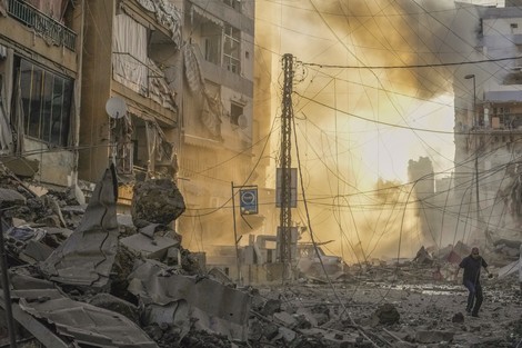 A man runs for cover as smoke raises in the background following an Israeli airstrike in Dahiyeh, suburb of Beirut, Lebanon, on Oct. 4, 2024. (AP Photo/Hassan Ammar)