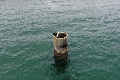 海面から突き出る、海底炭鉱「長生炭鉱」につながる円筒「ピーヤ」。調査初日はピーヤからダイバーが潜水して、内部を調べた＝山口県宇部市で2024年10月29日、小型無人機で後藤由耶撮影