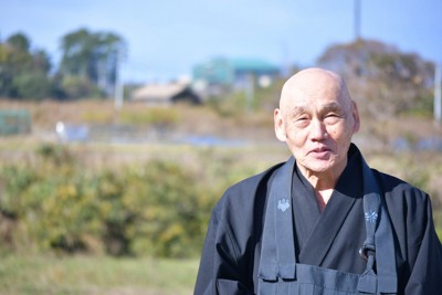 発電機の騒音の深刻さを語る村上正宏さん。後方の緑色の建屋にはXバンドレーダーが入っている＝京丹後市丹後町袖志で2024年11月28日正午、塩田敏夫撮影
