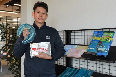 三日月形の冷却剤「くるっとクール」とタオルウオーマーで温める「バリアホット」を手にする山川大輔社長＝三重県松阪市大口町の三重化学工業で2024年12月18日、下村恵美撮影