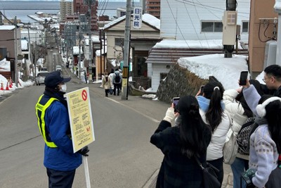 映画のロケ地にもなったJR小樽駅近くの「船見坂」で写真を撮る訪日外国人客（右手前）と注意を促す警備員＝北海道小樽市で2025年1月28日午前11時26分、谷口拓未撮影