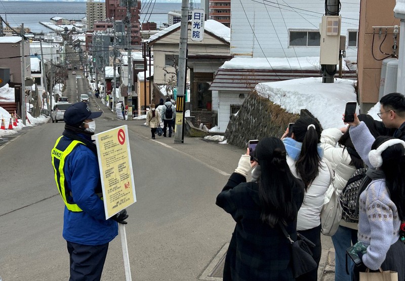 映画のロケ地にもなったJR小樽駅近くの「船見坂」で写真を撮る訪日外国人客（右手前）と注意を促す警備員＝北海道小樽市で2025年1月28日午前11時26分、谷口拓未撮影