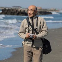 愛用のカメラを持って海岸を散策する嶋田洋さん＝千葉県旭市で2025年2月26日午前11時15分、近藤卓資撮影