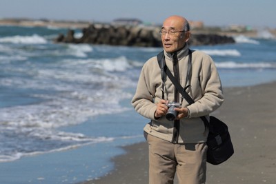 愛用のカメラを持って海岸を散策する嶋田洋さん＝千葉県旭市で2025年2月26日午前11時15分、近藤卓資撮影