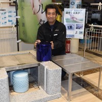 「遺骨シェルター壺」に手を添える藤島章弘社長。手前右と墓石の土台内側にセットされているのが「遺骨シェルター」＝静岡県沼津市一本松で2025年3月6日、丹野恒一撮影