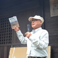 中間貯蔵施設内にある海渡神社の前で鎌田清衛さんは穏やかな声で古跡めぐりの参加者に地区の歴史を解説する。右手には自著「日隠山に陽は沈む」＝福島県大熊町で2024年8月10日午前10時40分、岩間理紀撮影