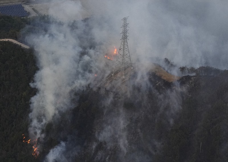山林火災の火と煙に包まれる鉄塔＝岡山市南区で2025年3月25日午後6時、本社ヘリから