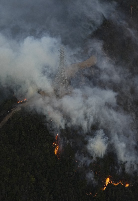 山林火災の火と煙に包まれる鉄塔＝岡山市南区で2025年3月25日午後6時、本社ヘリから