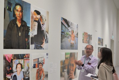 ベトナム戦争で手や足を失った人たちの写真を前に、来場者に解説する村山康文さん（左）＝京都市北区の立命館大国際平和ミュージアムで2025年4月14日午前10時11分