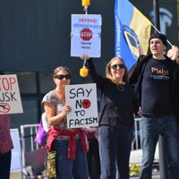 米電気自動車大手テスラの販売店前で「民主主義を守ろう」などと書かれたボードを車道に向けて掲げるデモ参加者＝ロンドンで2025年4月12日、福永方人撮影