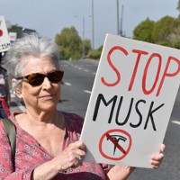 米電気自動車大手テスラの販売店前で「マスクを止めろ」と書かれたボードを車道に向けて掲げるデモ参加者＝ロンドンで2025年4月12日、福永方人撮影