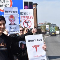 米電気自動車大手テスラの販売店前で「テスラをボイコットしろ」などと書かれたボードを車道に向けて掲げるデモ参加者＝ロンドンで2025年4月12日、福永方人撮影