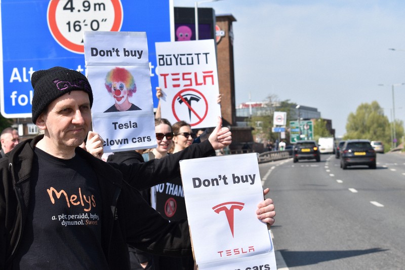 米電気自動車大手テスラの販売店前で「テスラをボイコットしろ」などと書かれたボードを車道に向けて掲げるデモ参加者＝ロンドンで2025年4月12日、福永方人撮影