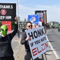 米電気自動車大手テスラの販売店前で「イーロン（・マスク氏）が嫌いならクラクションを」などと書かれたボードを車道に向けて掲げるデモ参加者＝ロンドンで2025年4月12日、福永方人撮影