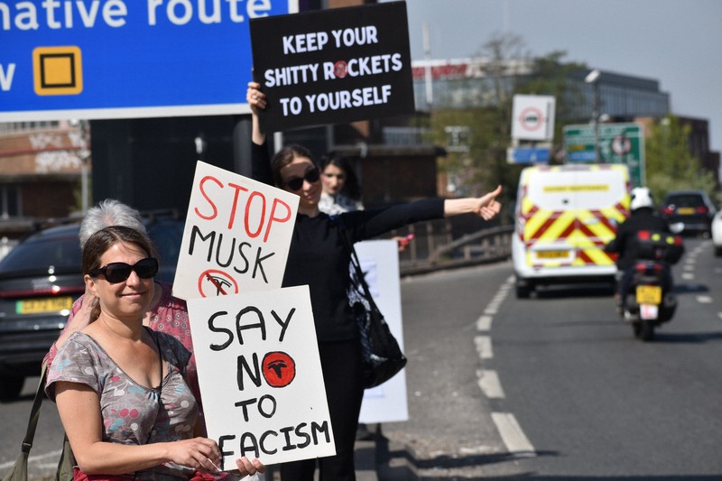 米電気自動車大手テスラの販売店前で「マスクを止めろ」などと書かれたボードを車道に向けて掲げるデモ参加者＝ロンドンで2025年4月12日、福永方人撮影