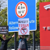 米電気自動車大手テスラの販売店前で「テスラをボイコットしろ」などと書かれたボードを車道に向けて掲げるデモ参加者＝ロンドンで2025年4月12日、福永方人撮影