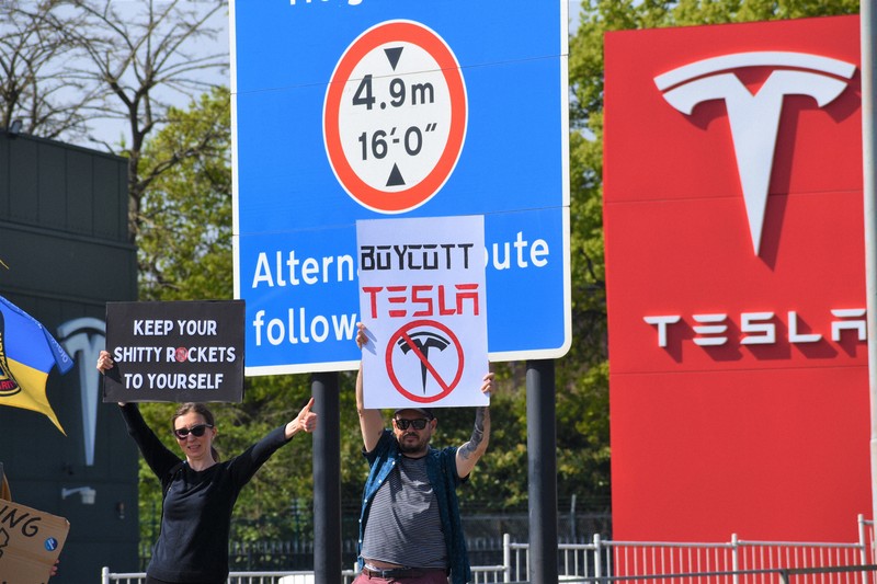 米電気自動車大手テスラの販売店前で「テスラをボイコットしろ」などと書かれたボードを車道に向けて掲げるデモ参加者＝ロンドンで2025年4月12日、福永方人撮影