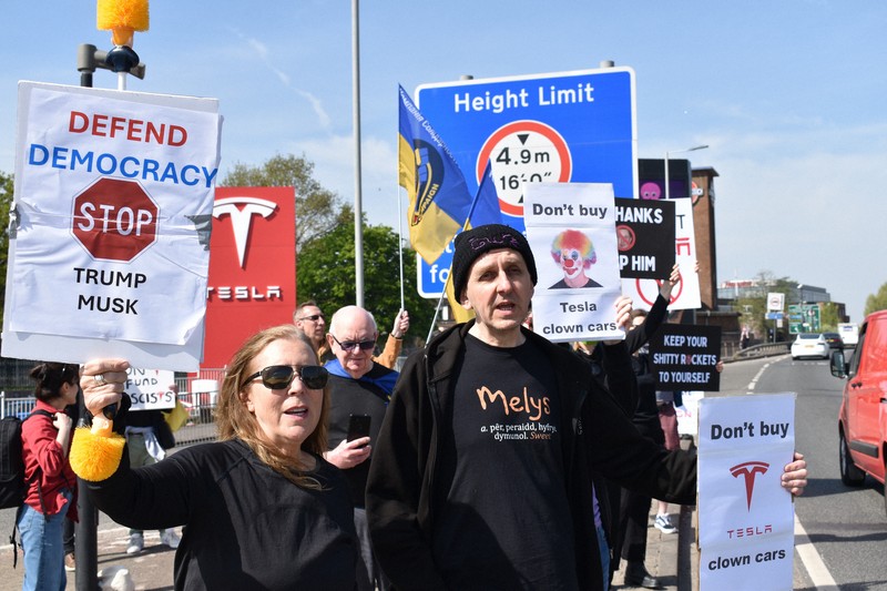 米電気自動車大手テスラの販売店前で「テスラを買うな」「トランプ、マスクを止めろ」などと書かれたボードを掲げるデモ参加者＝ロンドンで2025年4月12日、福永方人撮影
