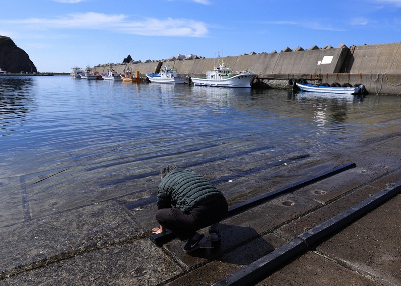 ウトロ漁港で海水に手を浸ける男性。男性の長男の小柳宝大さんは事故で行方不明となっている＝北海道斜里町で2025年4月23日午後2時7分、宮間俊樹撮影