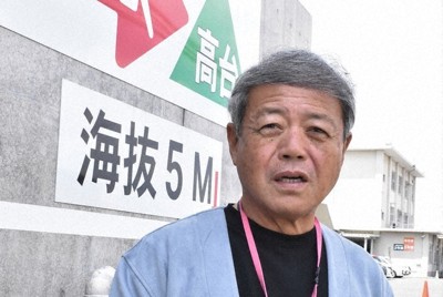 北星高校正門に掲げられた「命の矢印」の前に立つ坂田広峰さん＝三重県四日市市茂福で2025年4月16日、荒川基従撮影