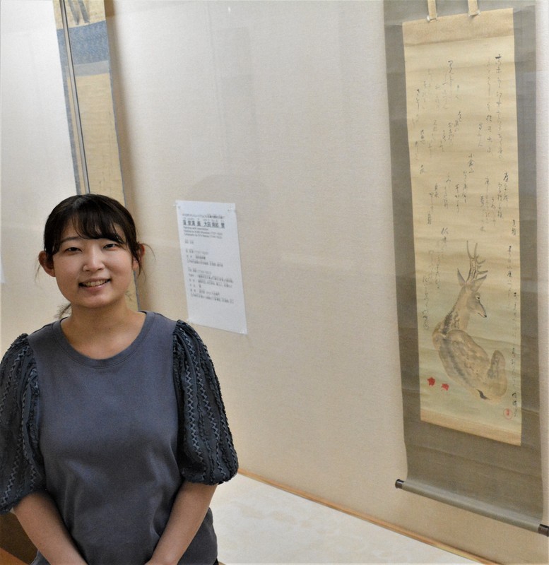 大田南畝が賛を寄せた絵を背景に「番組で親しんだ南畝の世界を深く味わえます」と話す谷川月彩学芸員＝愛媛県今治市の同市河野美術館で2025年6月5日、松倉展人撮影