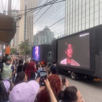 BTSのRMさんとVさんの除隊を祝い、所属するHYBE本社前に集まったファンら。2人を映し出した大画面のトラックが通過する度に歓声が上がった＝ソウル市内で2025年6月10日午前、堀山明子撮影